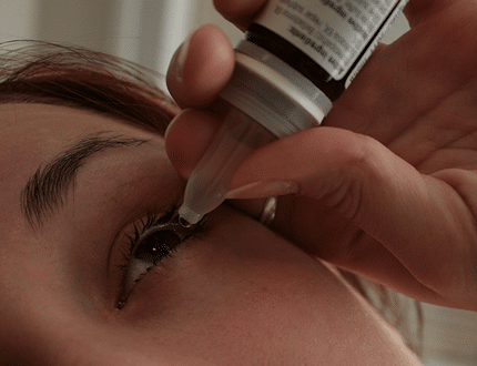A woman using eye drops medicine on her left eye