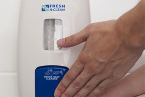 person dispensing toilet seat cleaner from a white dispenser