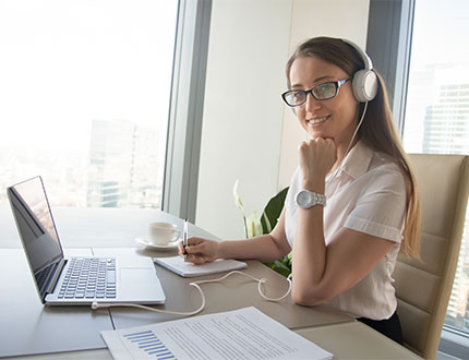 smiling female employee using a white headset while taking down notes