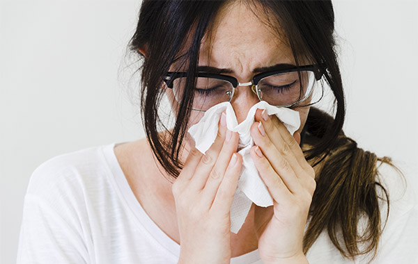 Close-up of a woman blowing her nose in tissue paper against white backdrop